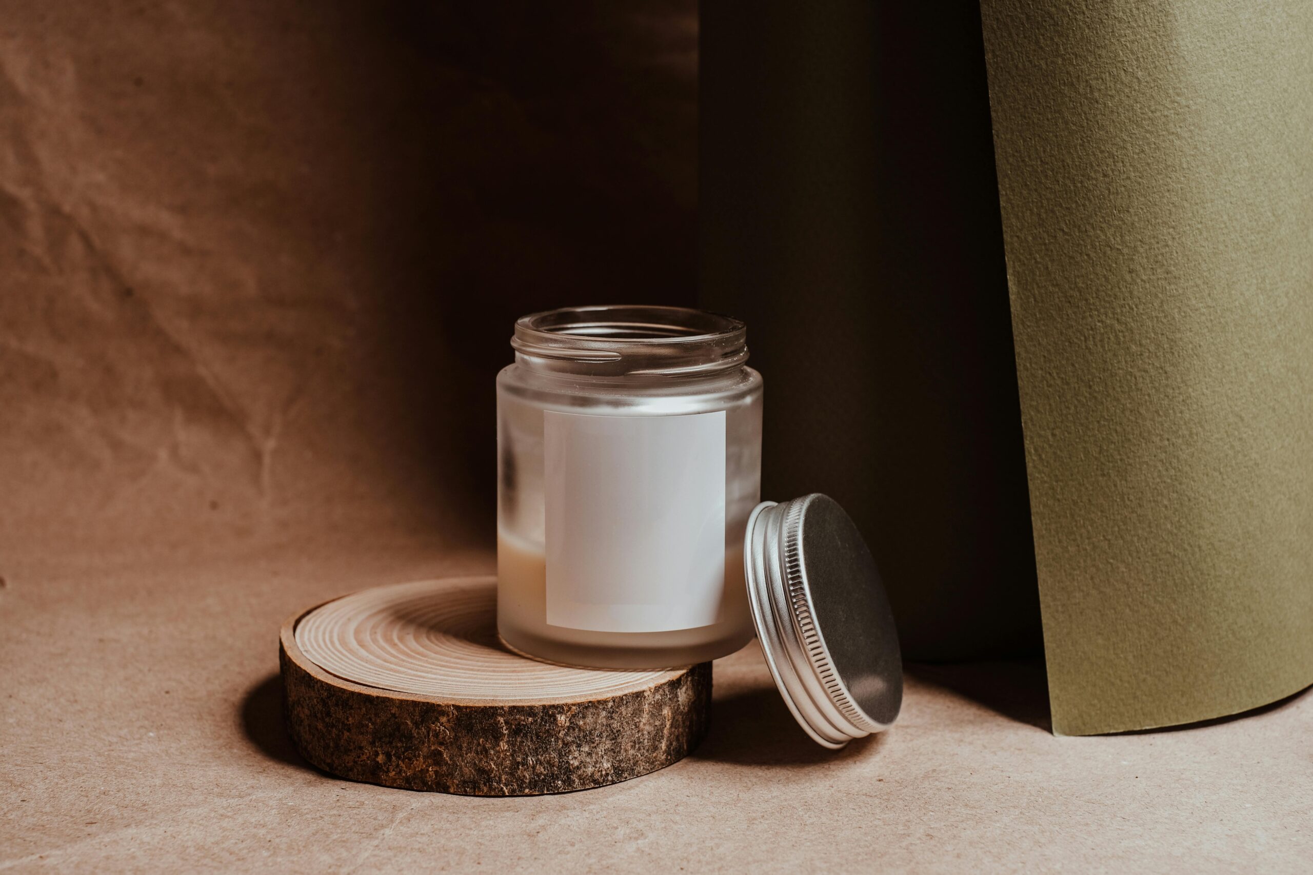 A minimalist candle in a glass jar with a metal lid, set on a wooden slice, creating a cozy ambience.