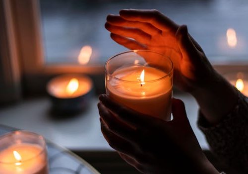 Warm candlelit ambiance with hands gently holding a burning candle indoors.